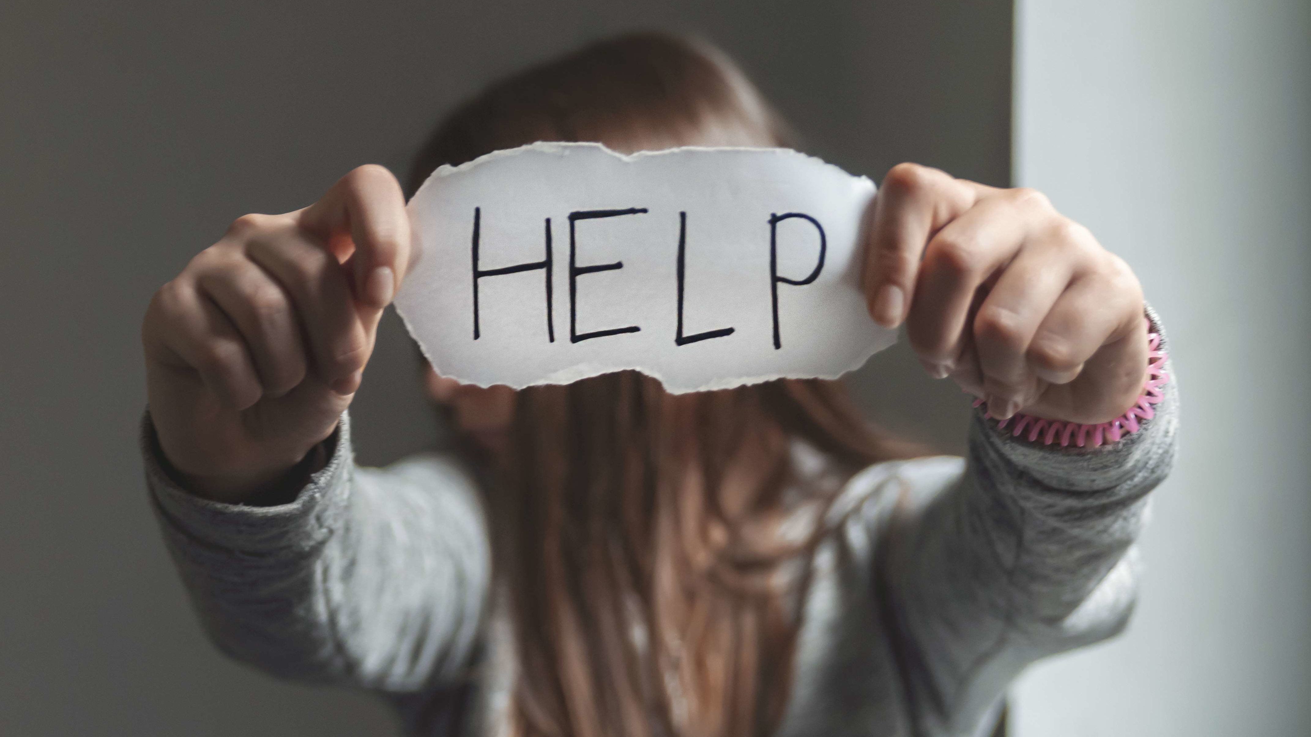 Help Ein Kind hält einen Zettel vor ihr Gesicht mit der Aufschrift "HELP" (HILFE).
