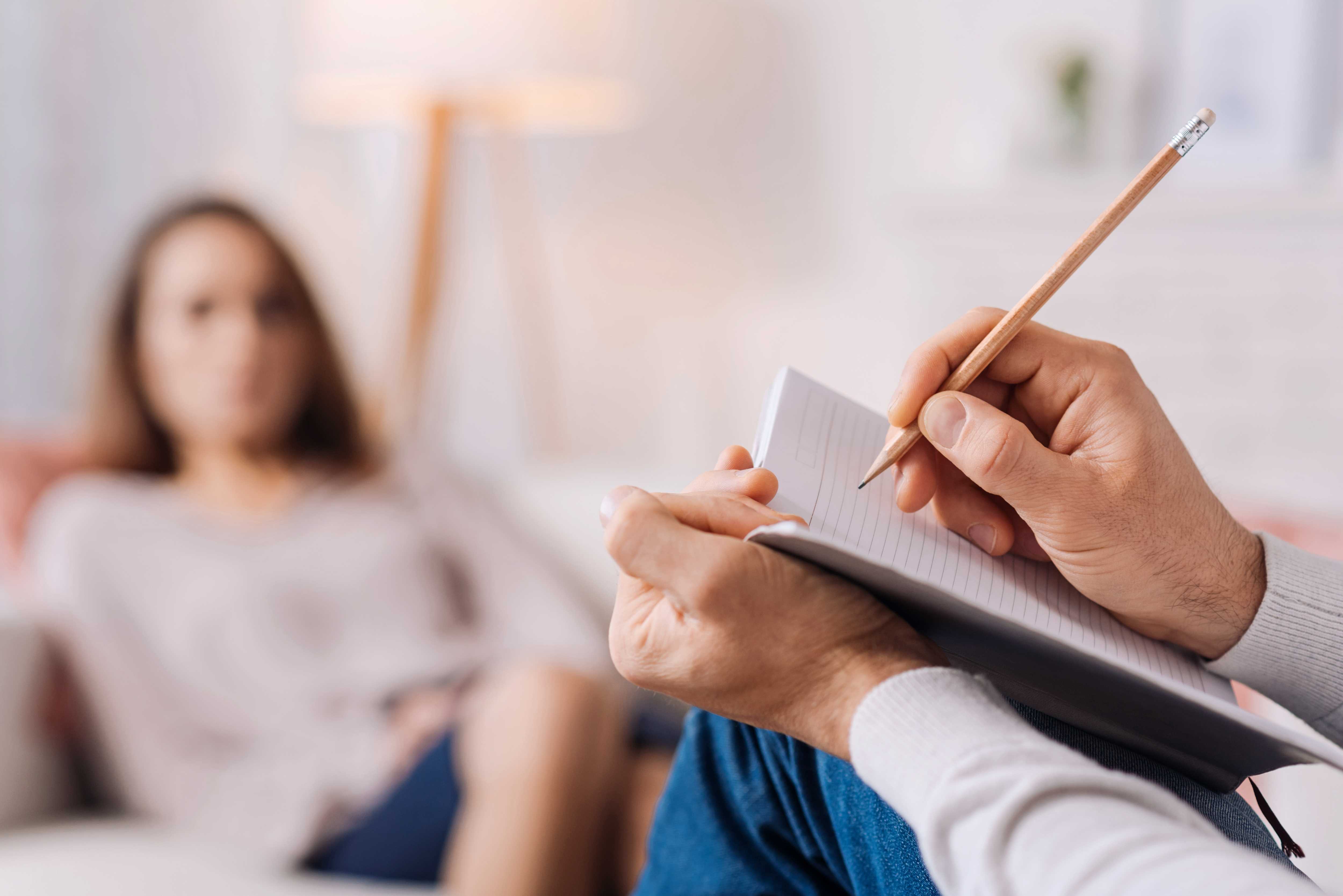 Frau in einer Beratung, im Vordergrund ein Berater, der in ein Buch schreibt