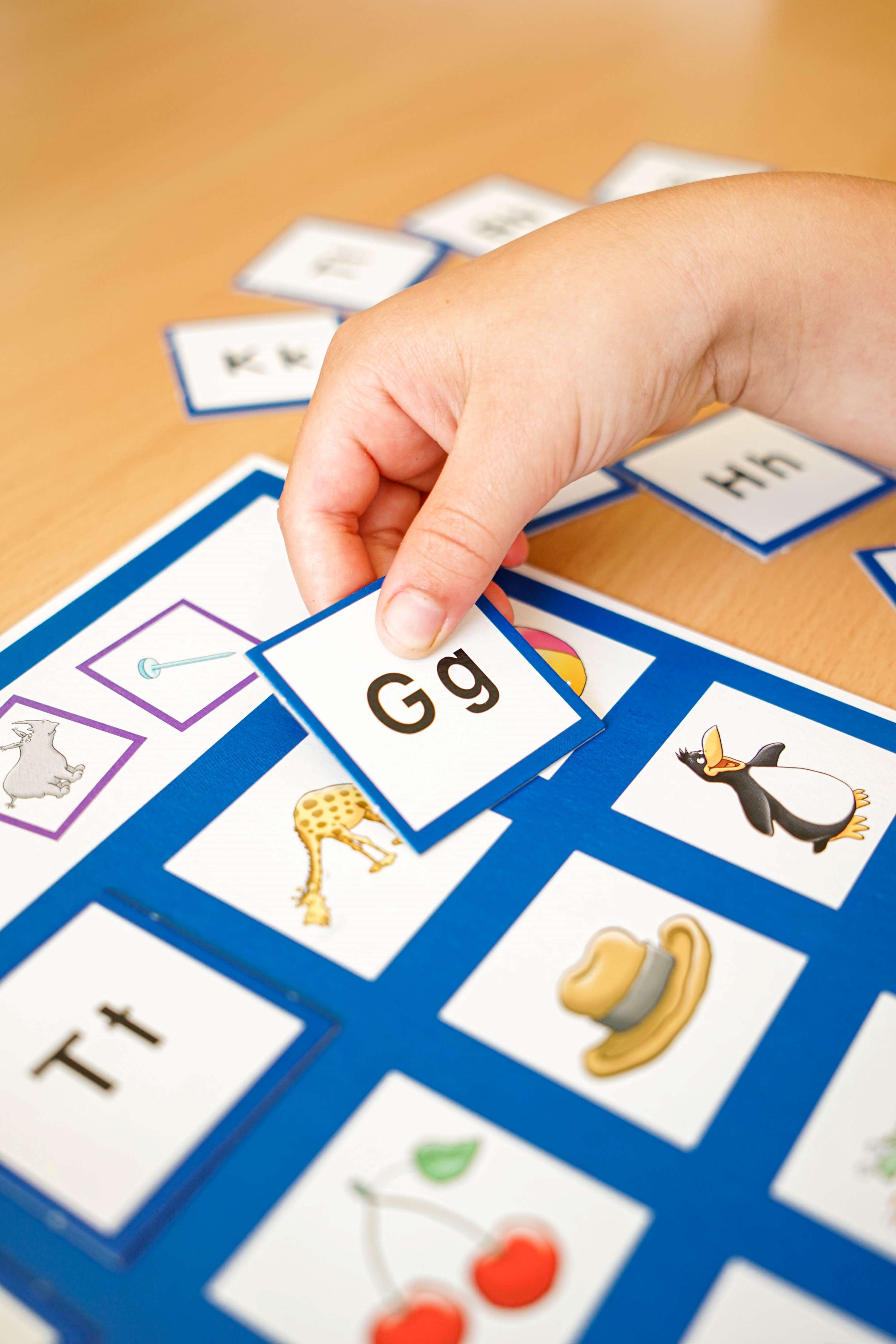 eine Hand eines Kindes, das mit Kärtchen spielt, auf denen Buchstaben zu sehen sind