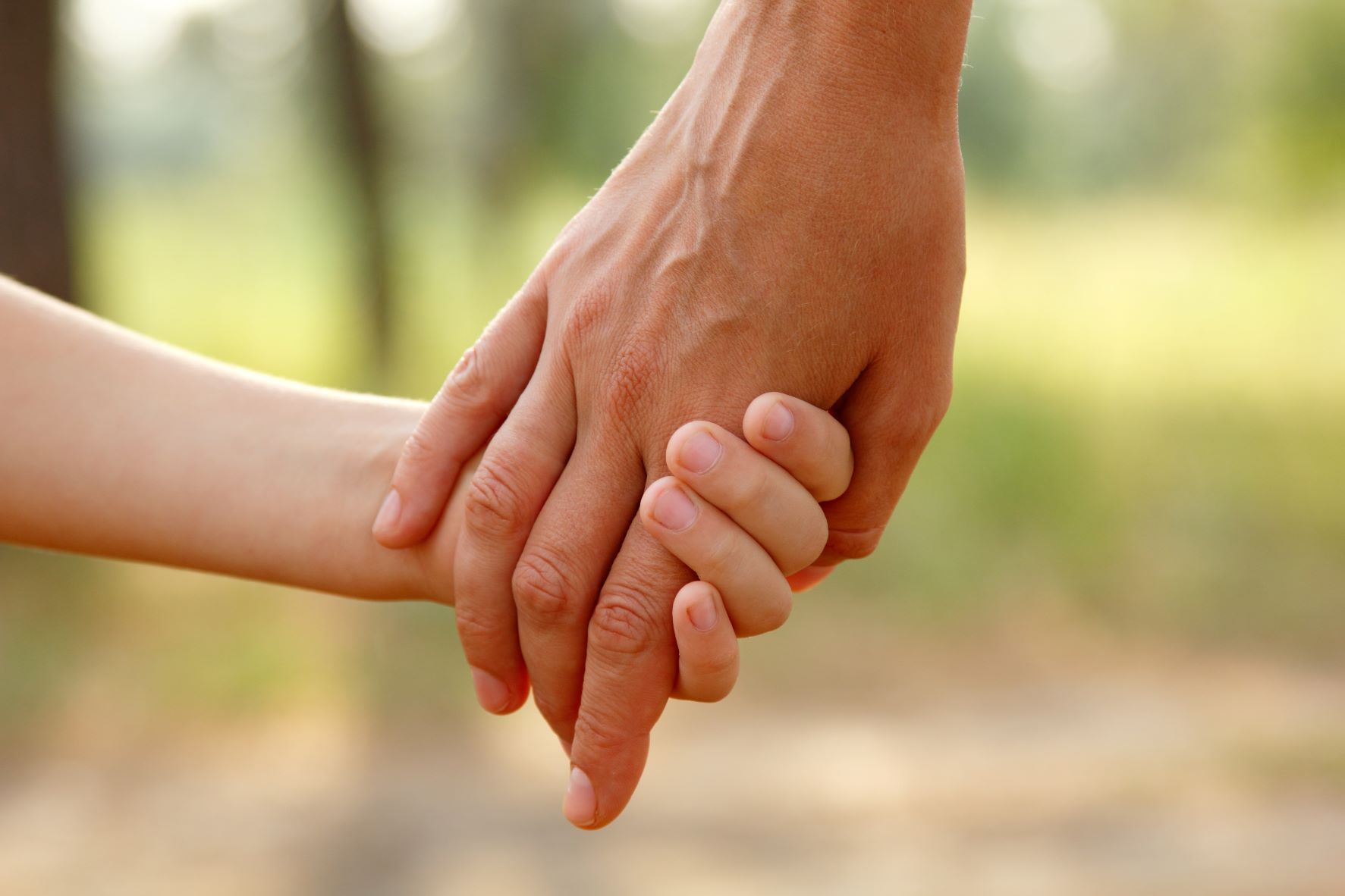 Besuchsbegleitung Ein Kind an der Hand eines Erwachsenen, draußen